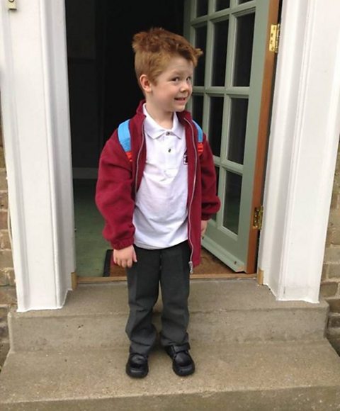 Rowan, a boy with autism and ADHD, standing in doorway on first day at mainstream primary school, wearing uniform.