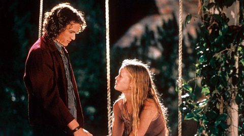 Heath Ledger, playing Patrick, holds hands with Julia Styles' Kat, who is sat on a swing, in a scene from 10 Things I Hate About You