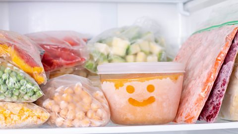 Packets of frozen veg in the fridge together with a tub of orange sauce with a smiley face on the side of it (made by fingers wiping through ice on the container)
