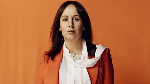 Jennifer Visser-Rogers stands against an orange background