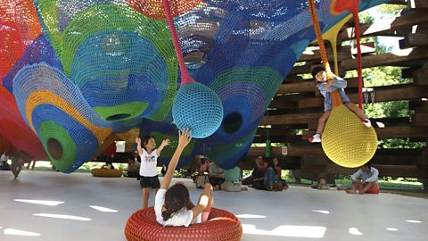 Children playing on a knitted net structure inside a wooden pavilion in Hakone, Japan.