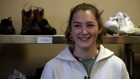 Costume trainee, Becca, stood in front of wardrobe items smiling to camera