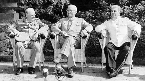 Three besuited men sit in wicker chairs in front of a microphone 