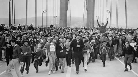 A crowd of people happily running the length of the Golden Gate Bridge in San Francisco to mark its official opening in 1937