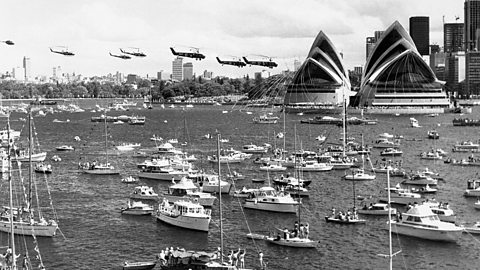 A black and white photograph from the opening day of Sydney Opera House with thousands of boats in the harbour while at least five army helicopters fly overhead