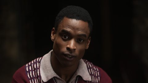 Actor Joshua Maynard, a young black man with very short curly hair, portrays D-Day soldier Allen Price. This is a close up shot of him against a dark background, and he is wearing a white collared shirt under a dark red jumper.