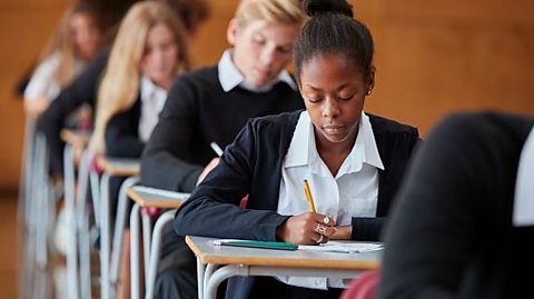 Students in uniform sit at exam desks writing