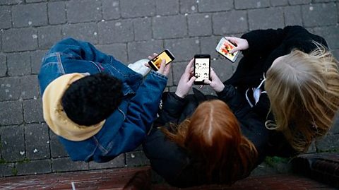 A view from above shows three teenagers looking at their phones