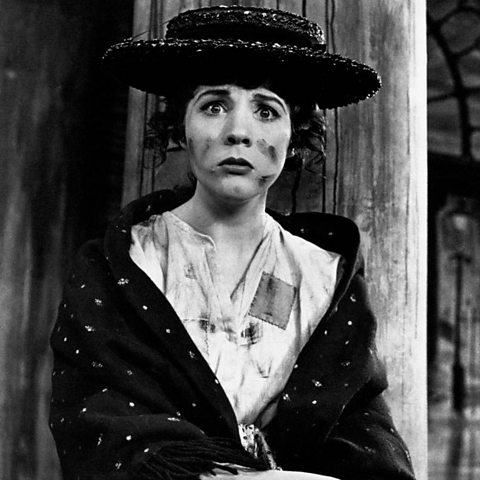 A young woman wearing a hat, worn shirt and shawl, with soot on her face