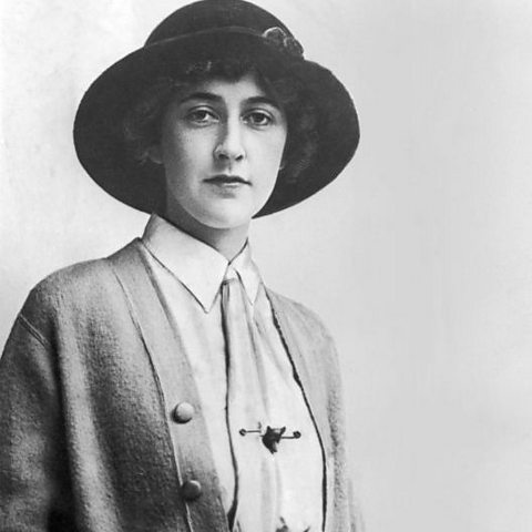 A standing young woman wearing a hat, long cardigan and shirt