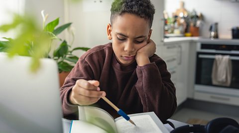 Pre-teen boy looks at a school book with pained and confused expression using a pen to help read the words line by line.