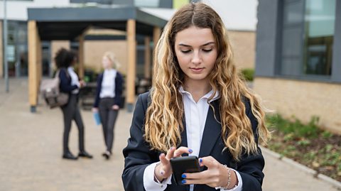 Girl in school uniform using smart phone outside a school.