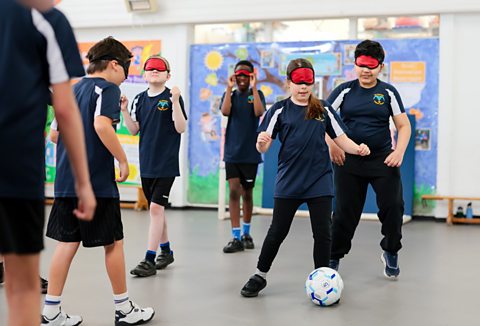 A group of primary school children wearing blindfolds while playing blind football