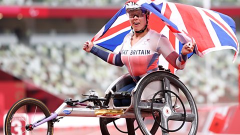 Hannah Cockroft holding a Union Jack flag seated in her racing wheelchair