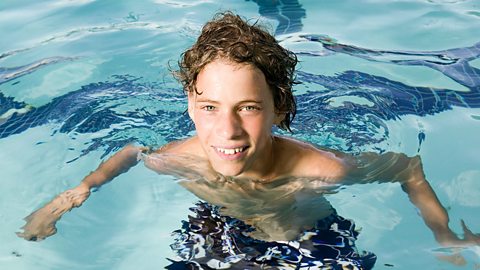 Boy swimming in a pool and smiling at the camera