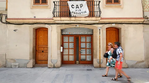 Getty Images A couple walking under a banner reading "No tourist flats" in Barcelona (Credit: Getty Images)