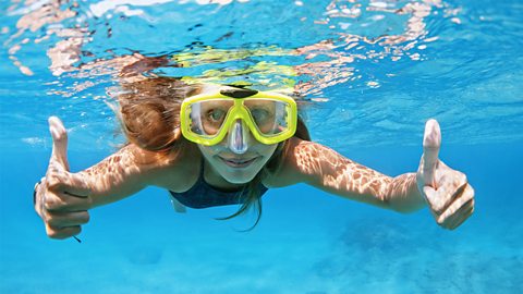 Girl smiling and putting her thumbs up underwater