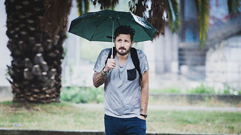 Grumpy looking man walking in the rain and holding up an umbrella