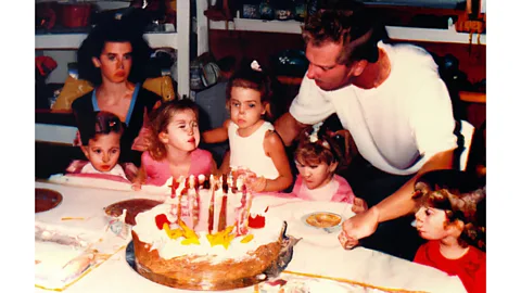 Maria Mavropoulou Uma menina de 5 anos soprando as velas do seu bolo de aniversário com toda a família ao seu redor em uma festa na Grécia, década de 1990 (Crédito: Maria Mavropoulou)