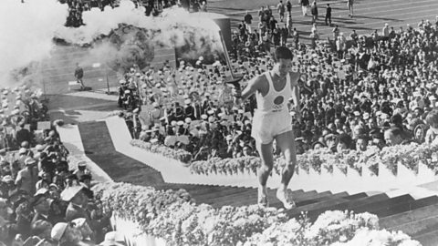 A young man carries the torch up the stairs to light the Olympic cauldron in a crowded stadium.