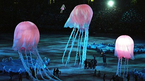 Giant inflatable jellyfish float over a stage in the darkness, glowing.