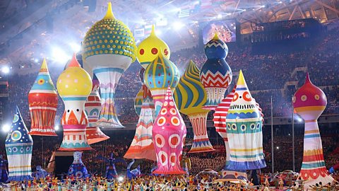 Giant, colourful inflatable domes being carried by hundreds of people in a lit up arena.