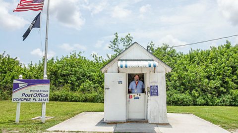 A clerk stands in a small post office shack. 