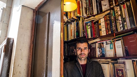 Simão Carneiro stands by in front of a book case