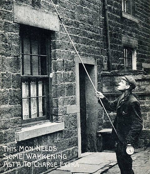 A knocker upper goes about his work, 1920s.