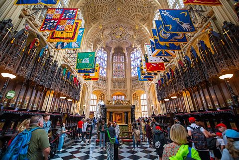 Lady Chapel in Westminster Abbey, arched decorative ceiling, chequered floor, banners of coats of arms above heads of visitors