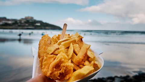 A portion of fish and chips with the seaside behind it