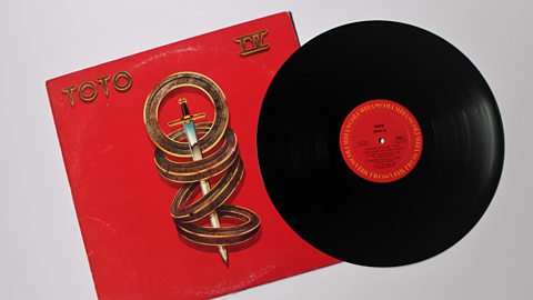 A red record album cover with titled Toto IV.  The image on the cover is a sword with 4 gold rings around it.  A black record with red label is to the right of the cover..