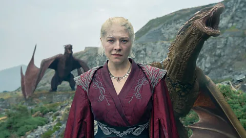 Emma D'Arcy dans le rôle de la princesse Rhaenyra Targaryen dans House of the Dragon, se tient devant deux dragons (Crédit : Theo Whiteman/ HBO)