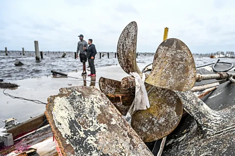 Getty Images Broken rusted boat rudder by the shoreline, near two people (Credit: Getty Images)