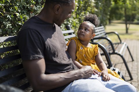 Father and daughter sitting on a park bench having a conversation. 