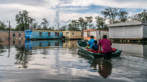 Getty Images People on a small boat wading through flood waters in a neighbourhood (Credit: Getty Images)