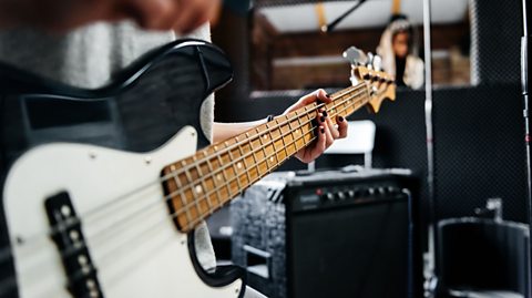 A close up image of a white and black bass guitar being played on a stage.