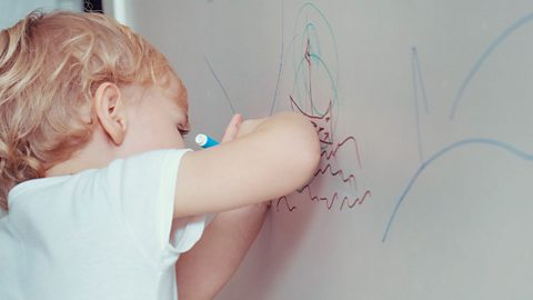 Young child drawing on the wall with markers.