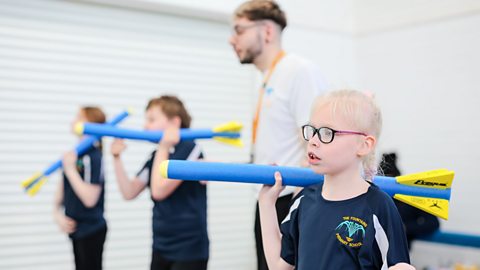 Children aiming to throw javelins with teacher supporting them