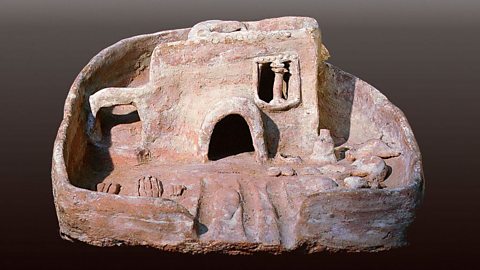 A clay sculpture of a double storey house, with a window, door and archway