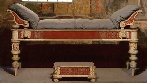 An ancient Roman bed with red panels, ornate legs and carved lions