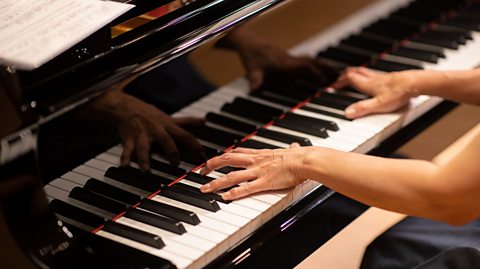 A close up of the lower range of a piano with the hands of a pianist playing.