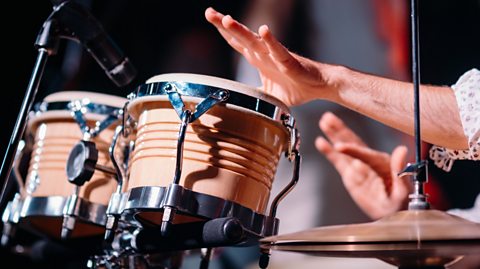 Close up photo of a man's hands playing percussion bongo drums by a microphone.