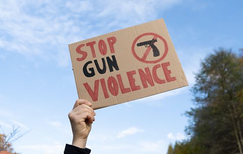 Hand holding sign with slogan Stop Gun Violence, black pistol strikethrough.