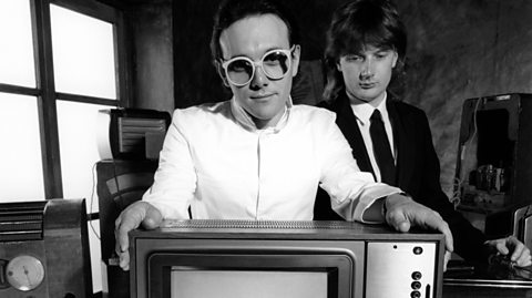 A black and white image of The Buggles standing next to a television set 