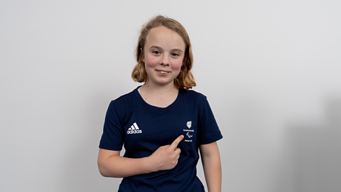 ParalympicsGB swimmer Iona Winnifrith smiling and pointing to the ParalympicsGB logo on her T-shirt