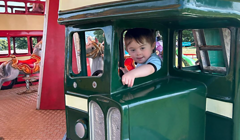 Parker, a toddler with Down's syndrome, rides a bus on a fairground carousel.