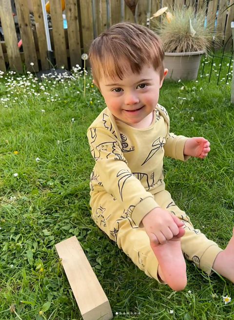 Parker smiling in the garden - sitting on the grass with a building block by his side.