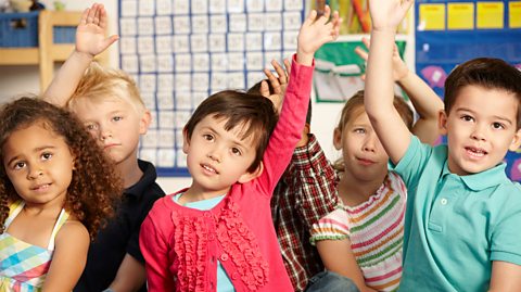 A group of nursery age kids with their hands up to ask a question