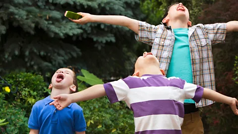 Getty Images Three boys with tongues out/ heads up to taste the rain, green bushes in background (Credit: Getty Images)